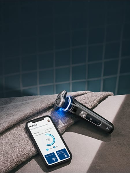 Oparty o ręcznik smartfon z włączoną aplikacją na monitorze. Obok golarka ze świecącym niebieskim ringiem.