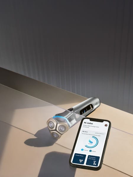 Na szklanej powierzchni smartfon z włączoną aplikacją na monitorze. Poniżej golarka leżąca na stole.