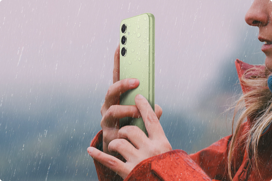 phpwgs8ba sm-a546-09-2-ip67 Kobieta robi sobie zdjęcie w deszczu z Galaxy A54 5G w kolorze limonkowym.