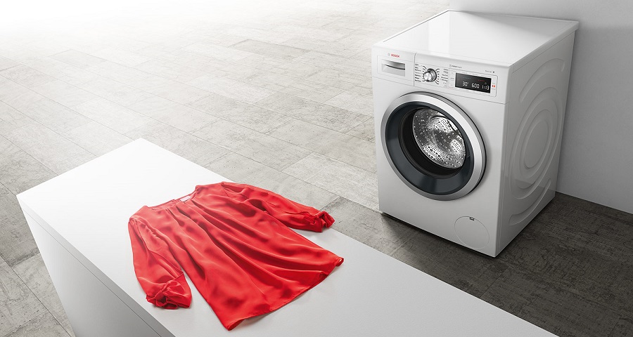 Сушильная машина Bosch рядом с красной блузкой на белой столешнице.