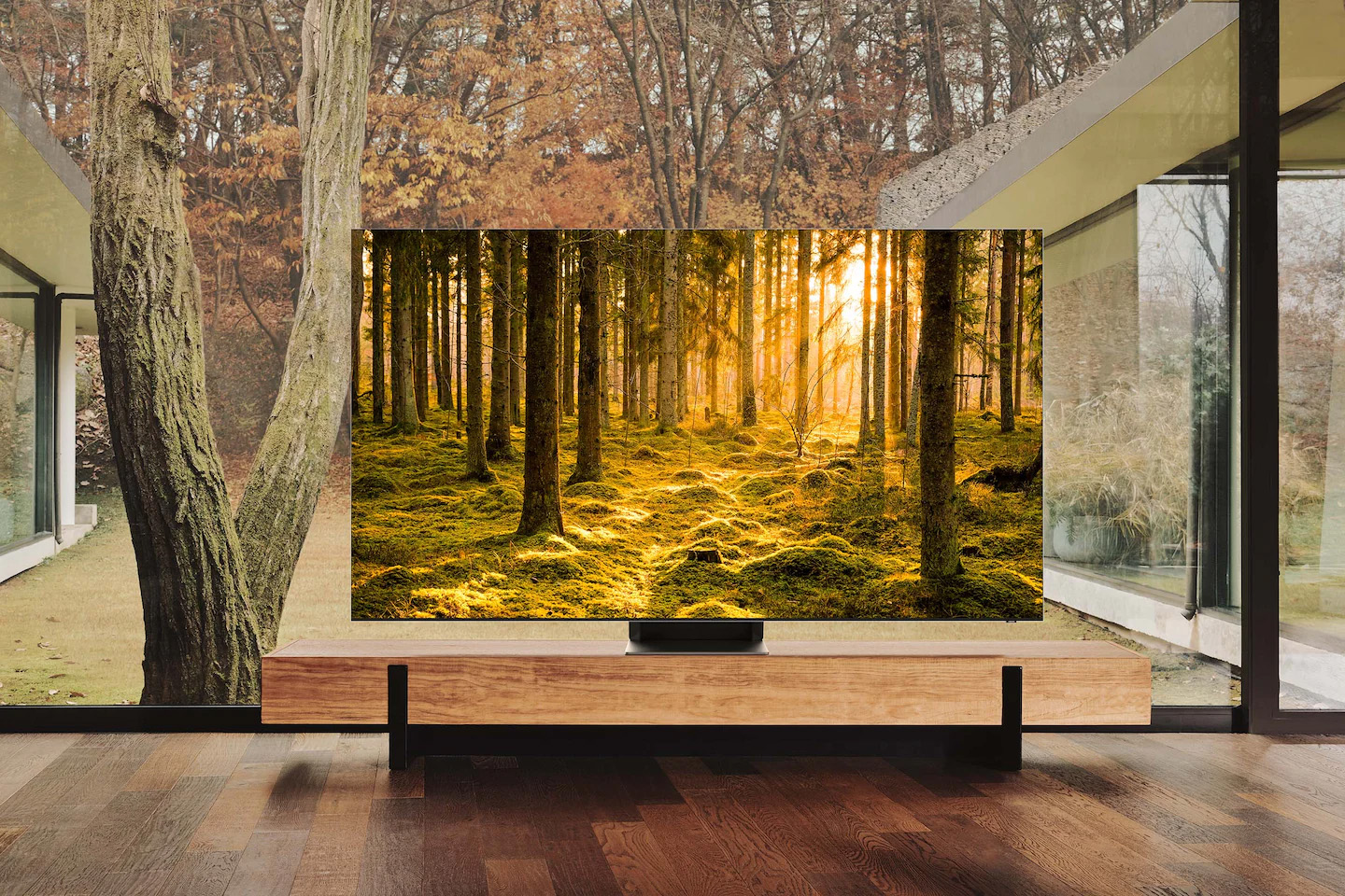 Telewizor QLED 8K Excellence Line Samsung na szafce stojący na tle okna z widokiem na las. QN700BTXXH
