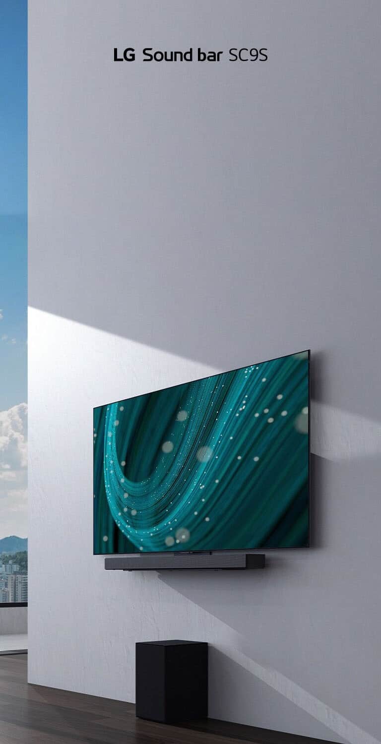 Telewizor i soundbar LG SC9S wiszą na białej ścianie. Pod nimi na podłodze stoi czarny bezprzewodowy subwoofer. Za oknem po lewej stronie widać panoramę miasta i niebieskie niebo.