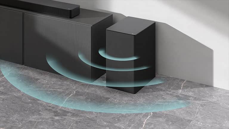 Soundbar stoi na szafce. Obok na podłodze stoi bezprzewodowy subwoofer. Z subwoofera wydobywają się niebieskie fale dźwiękowe.