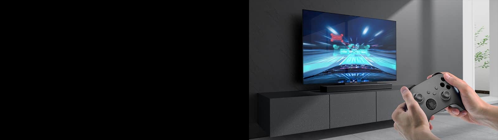 Soundbar stoi na szafce, a na ekranie podłączonego do niego telewizora jest wyświetlona scena z gry wyścigowej. Konsola do gier znajduje się na dole po prawej stronie obrazu i jest trzymana w dwóch dłoniach.