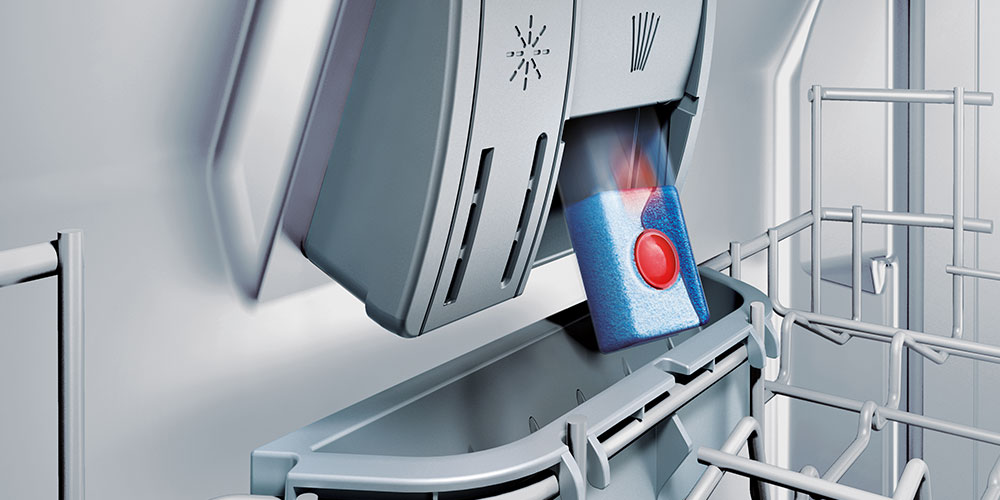 Tabletka do zmywarki z czerwonym środkiem wpada do dozownika wewnątrz urządzenia.