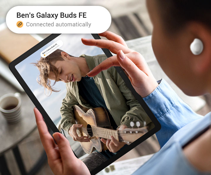 Osoba używa Galaxy Tab A9+ ze słuchawkami Galaxy Buds FE. Na ekranie widać mężczyznę grającego na gitarze. Na górze wyświetlacza widoczne jest powiadomienie i powiększona wersja tego samego powiadomienia w lewym górnym rogu. Powiadomienie dotyczy słuchawek Buds Galaxy Buds FE, a następna linia posiada ikonę połączenia z tekstem Połączone automatycznie.
